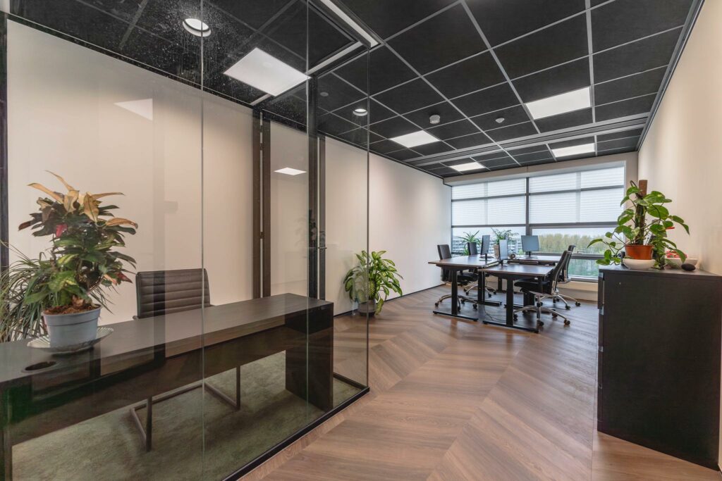 Modern kantoorinterieur aan de Joop Geesinkweg met glazen vergaderruimte, bureaus en groene kamerplanten.